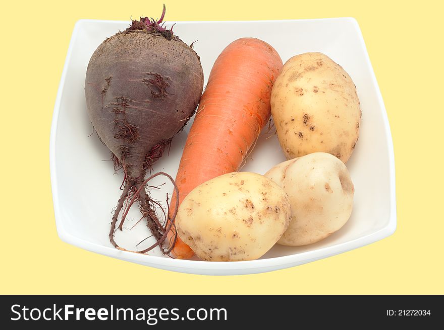 Crude beet, carrots, potato on a plate close up are isolated. Crude beet, carrots, potato on a plate close up are isolated