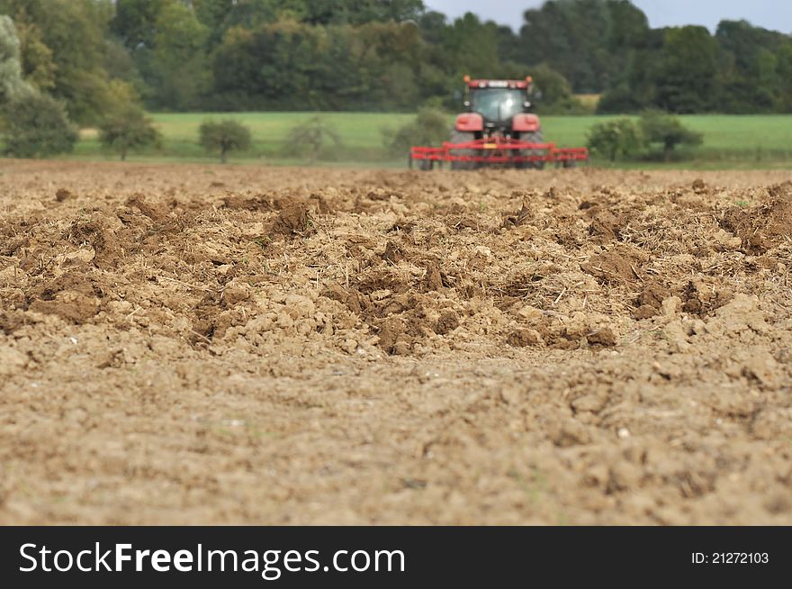 Plowed field in the foreground in front of a tractor in the distance. Plowed field in the foreground in front of a tractor in the distance