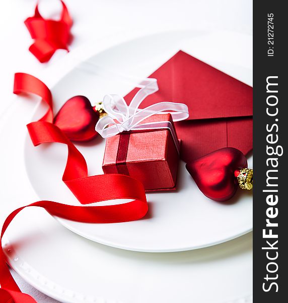 Close up of a little red gift box, envelope and christmas ornaments on white plates. Close up of a little red gift box, envelope and christmas ornaments on white plates