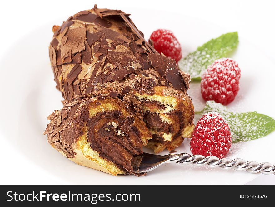 Miniature chocolate swiss roll cake served on a plate with mint leaves and raspberries on white background