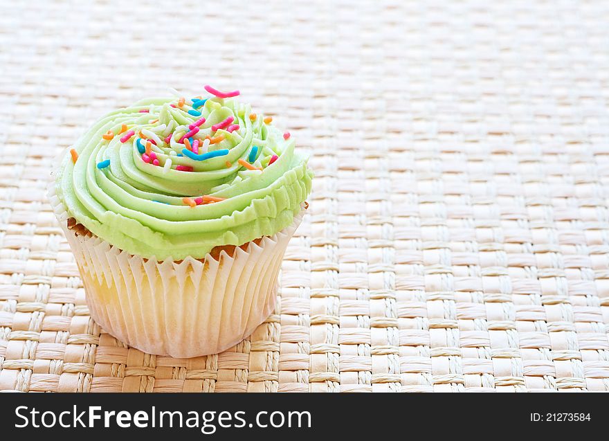 Fresh vanilla cupcake with lime icing on woven straw background