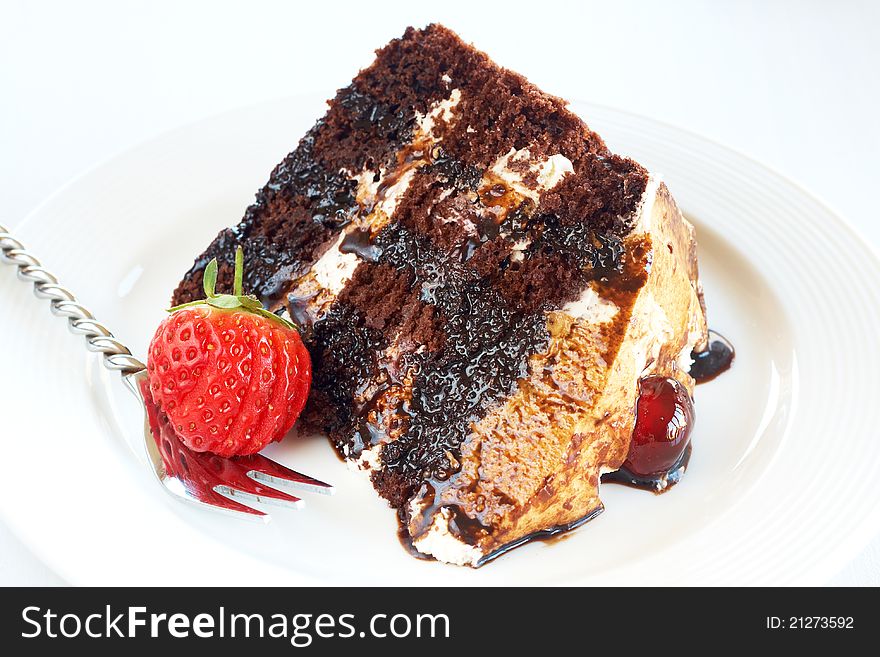 Slice of Black Forest cake with fresh cream and cherries, served on a white plate with silver fork