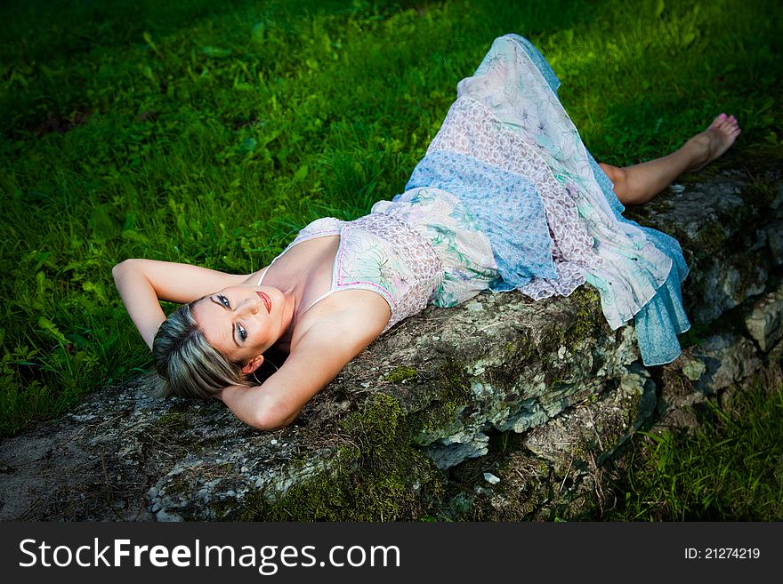 Portrait of attractive woman in blue sundress lying on stones against natural landscape at summer morning. Portrait of attractive woman in blue sundress lying on stones against natural landscape at summer morning