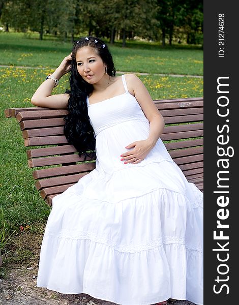 Beautiful pregnant girl sitting on bench in park