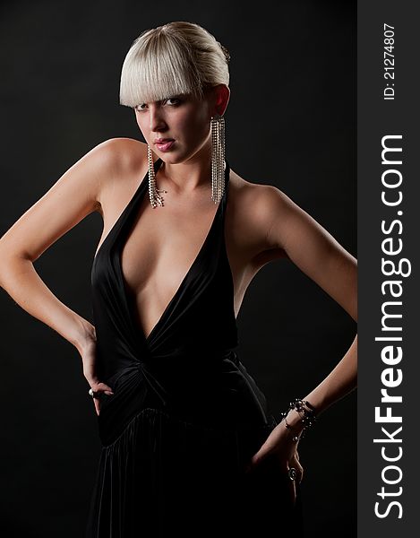 Photo of glamour model in an elegant black dress and beautiful jewelry posing in studio. Photo of glamour model in an elegant black dress and beautiful jewelry posing in studio