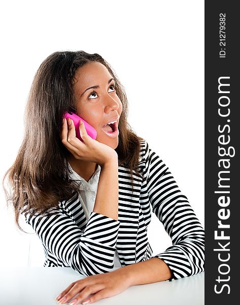 Description Teenage girl on a pink cell phone listening and looking shocked at a desk. Description Teenage girl on a pink cell phone listening and looking shocked at a desk