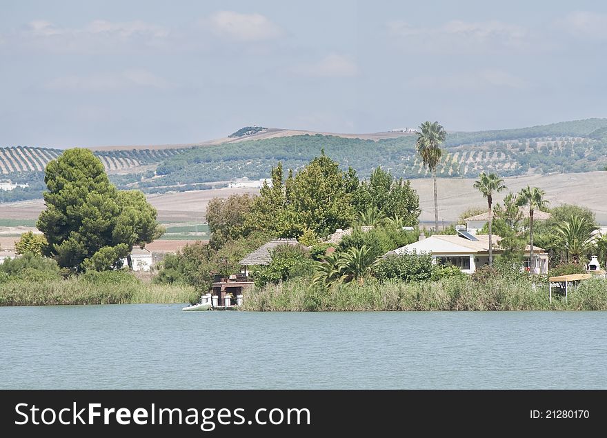 House on the shore of a lake surrounded by palm trees and vegetation located in the Spanish town of Arcos de la Frontera, fields are the background, on a cloudy day