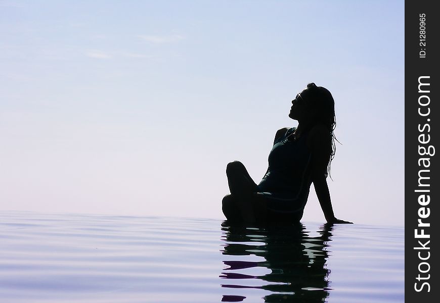 A silhouette of a woman basking in the Sun at the pool, during the early hours.