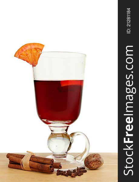 Glass of mulled wine with a slice of orange and spices on a wooden surface against a white background