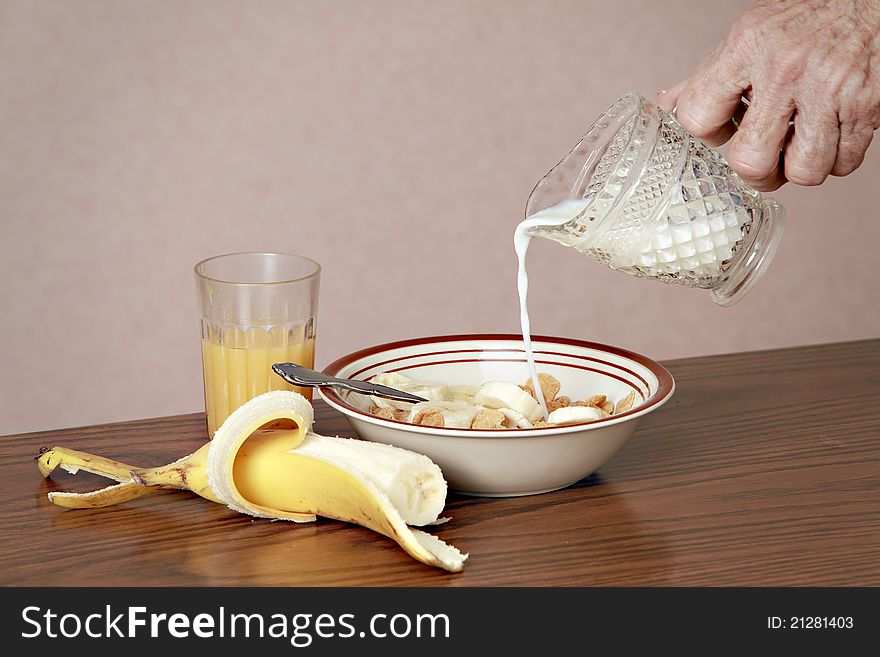 Male hand pouring milk into breakfast cereal. Orange juice and banana on table.