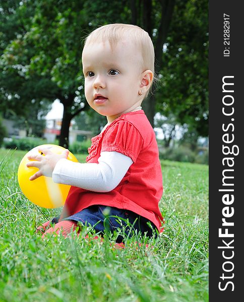 Cute little girl playing with yellow ball on the meadow