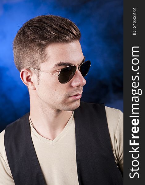 Handsome young male model with aviator sunglasses before a blue smoke background. Handsome young male model with aviator sunglasses before a blue smoke background.