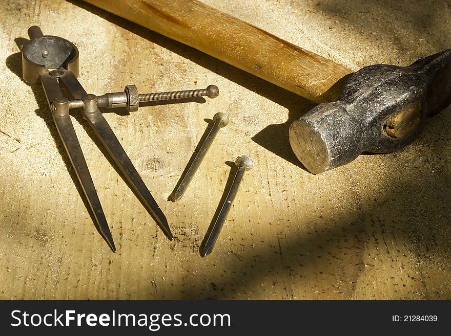 A hammer laying next to nails and a drafting compass with selective focus and selective light. A hammer laying next to nails and a drafting compass with selective focus and selective light.