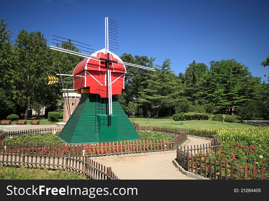 A red windmill on a grassplot in a park.