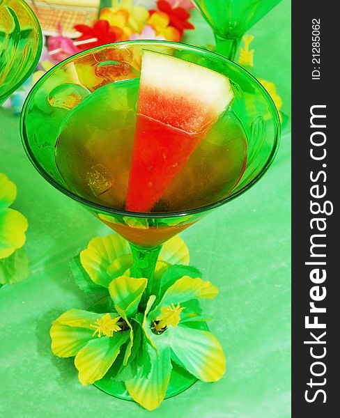 A cup of watermelon martini in green glass with flower.