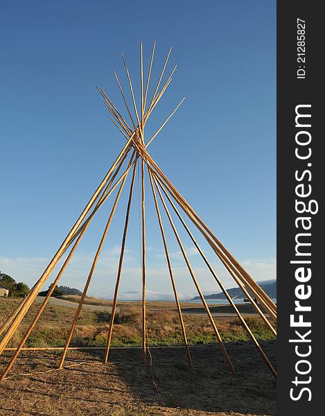 A teepee is beeing build in a field with no cover yet. A teepee is beeing build in a field with no cover yet.