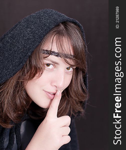 Woman in black hood puts forefinger to lips as a sign of silence on white background. Woman in black hood puts forefinger to lips as a sign of silence on white background