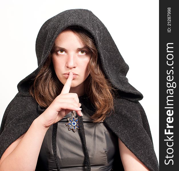 Woman in black hood puts forefinger to lips as a sign of silence on white background. Woman in black hood puts forefinger to lips as a sign of silence on white background