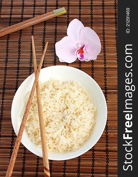 An Asian place setting consisting of a bowl of white rice with chopsticks and a pretty orchid. View from above. An Asian place setting consisting of a bowl of white rice with chopsticks and a pretty orchid. View from above.