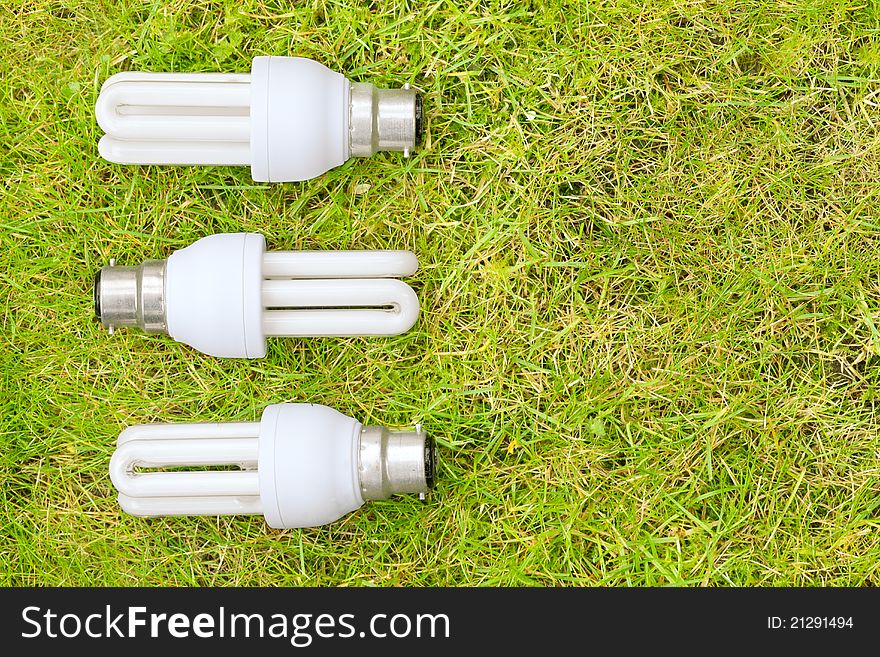 Three energy saving light bulks arranged in a pattern on some grass. Symbolising green energy. Three energy saving light bulks arranged in a pattern on some grass. Symbolising green energy.