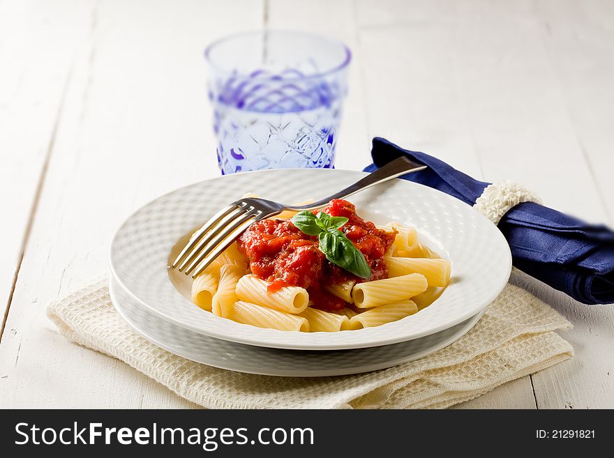 Photo of delicious pasta with basil and tomato sauce on white wooden table. Photo of delicious pasta with basil and tomato sauce on white wooden table