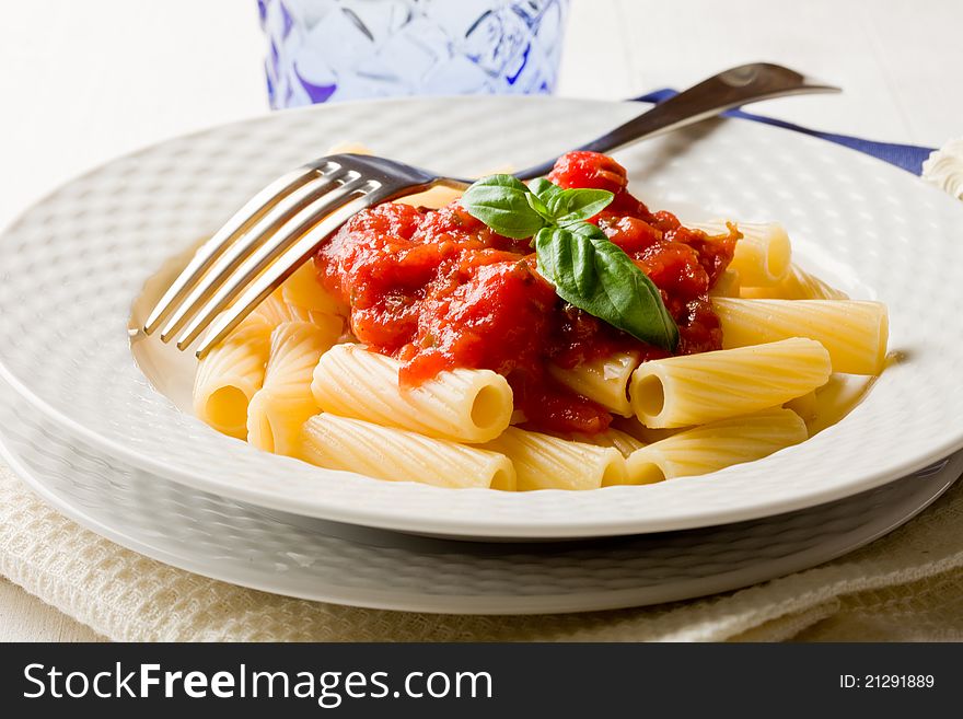 Photo of delicious pasta with basil and tomato sauce on white wooden table. Photo of delicious pasta with basil and tomato sauce on white wooden table