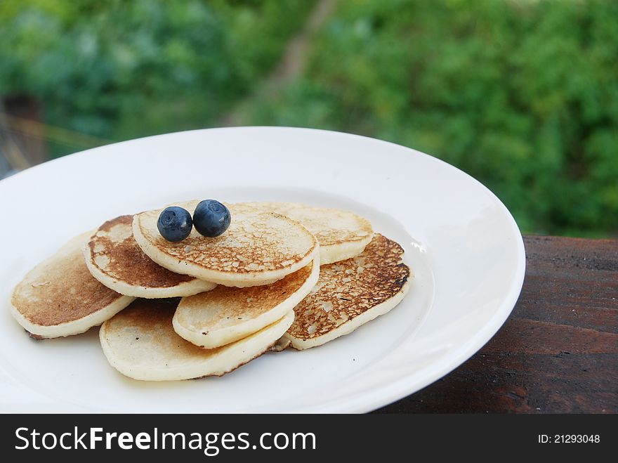 Thick pancakes with fresh blueberries on a white plate for breakfast outdoors. Thick pancakes with fresh blueberries on a white plate for breakfast outdoors