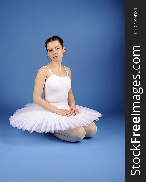 Ballet dancer sitting in white tutu against the blue background
