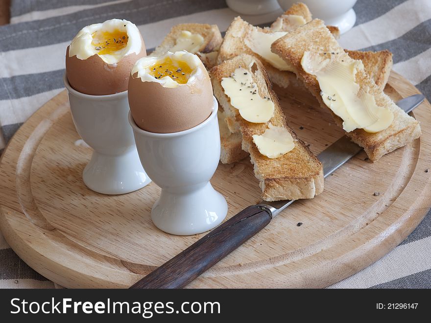 Soft-boiled eggs with buttered soldiers on a wooden board. Soft-boiled eggs with buttered soldiers on a wooden board