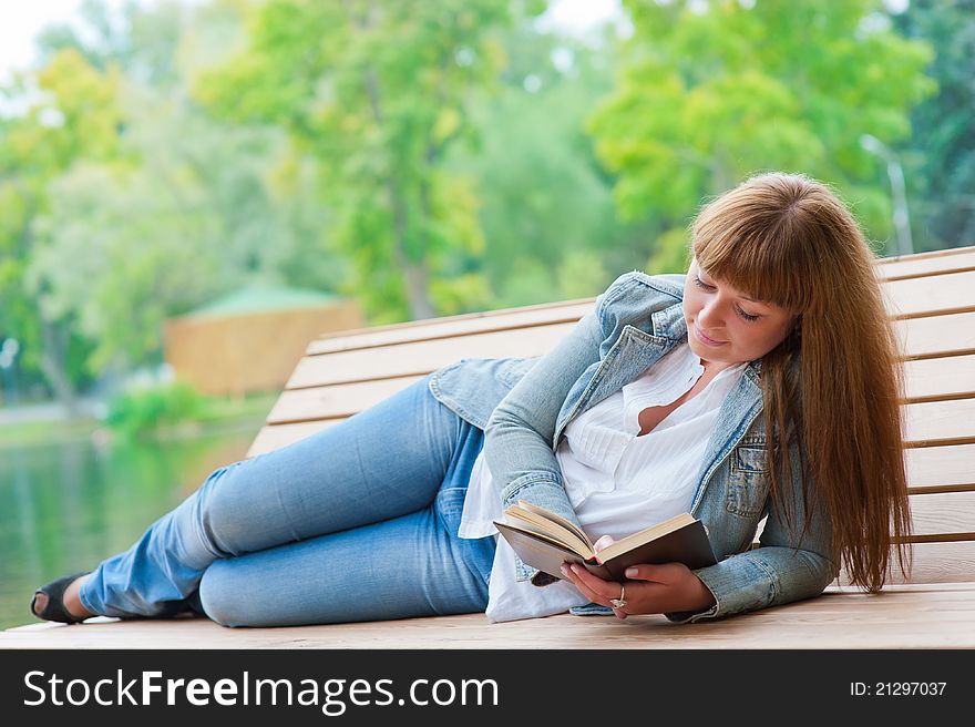 Young woman reading a book lying on the bench in the park. Young woman reading a book lying on the bench in the park