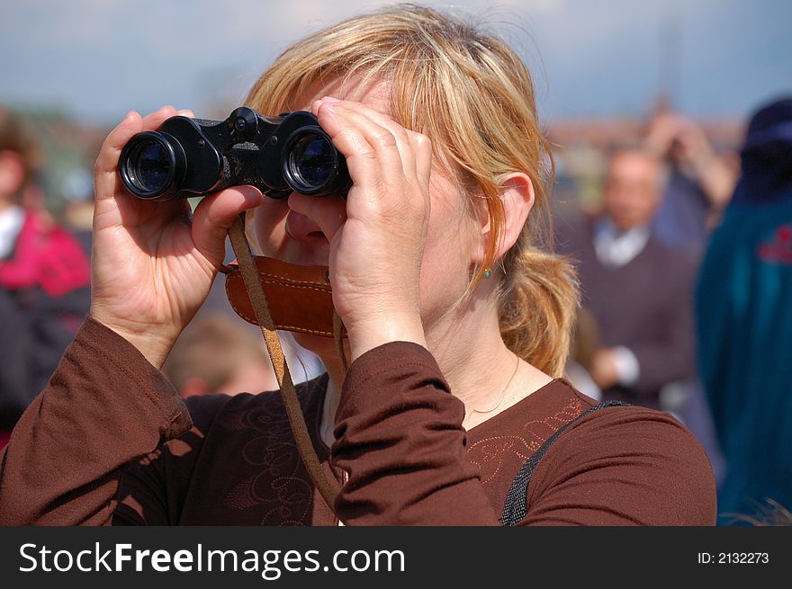 Woman with binoculars observing distant events, surrounded by crowd. Woman with binoculars observing distant events, surrounded by crowd.