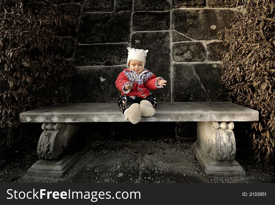 Little boy smiles, sits on stone bench with cup and a piece of stick