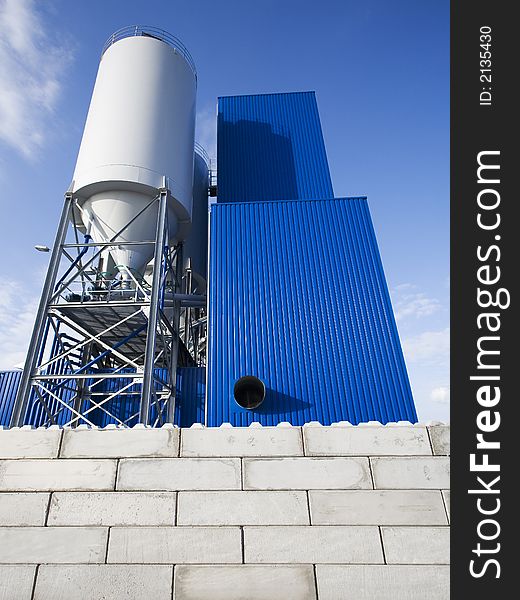 Blue and white industrial buildings including grain or sand silos against blue sky