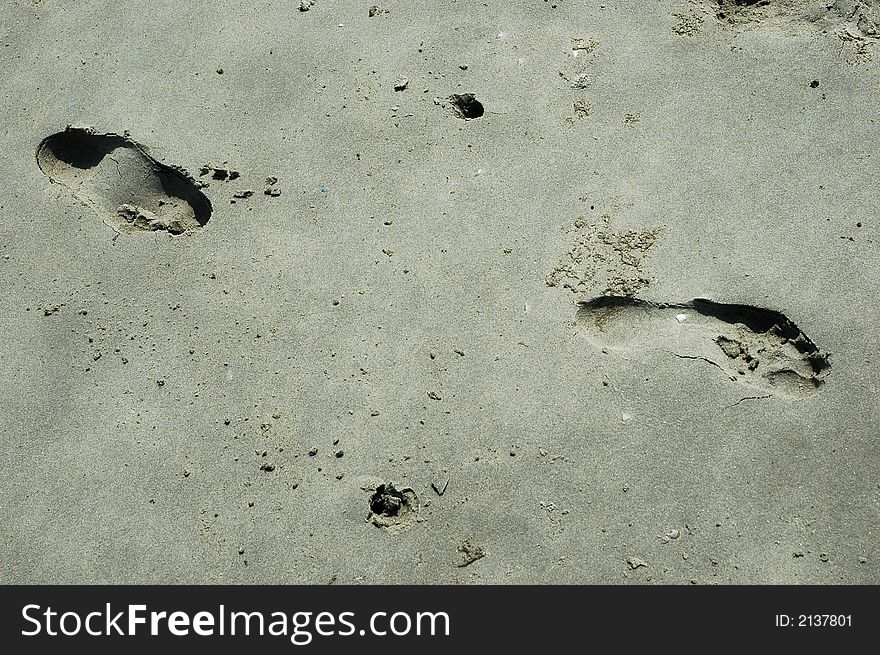 Two footsteps in the sand together with two marks of nordic walking sticks.