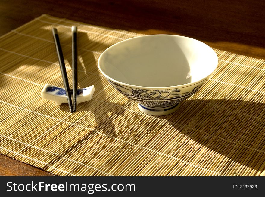 Chinease bowl with chopstick rest and chopsticks on bamboo place mat. Chinease bowl with chopstick rest and chopsticks on bamboo place mat