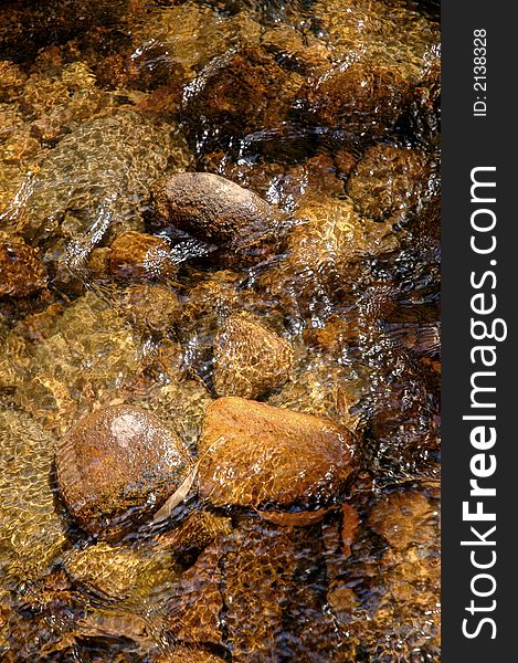 The crystal clear running water over the rocks of a mountain creek bed with gilmmering reflections from the sun in it