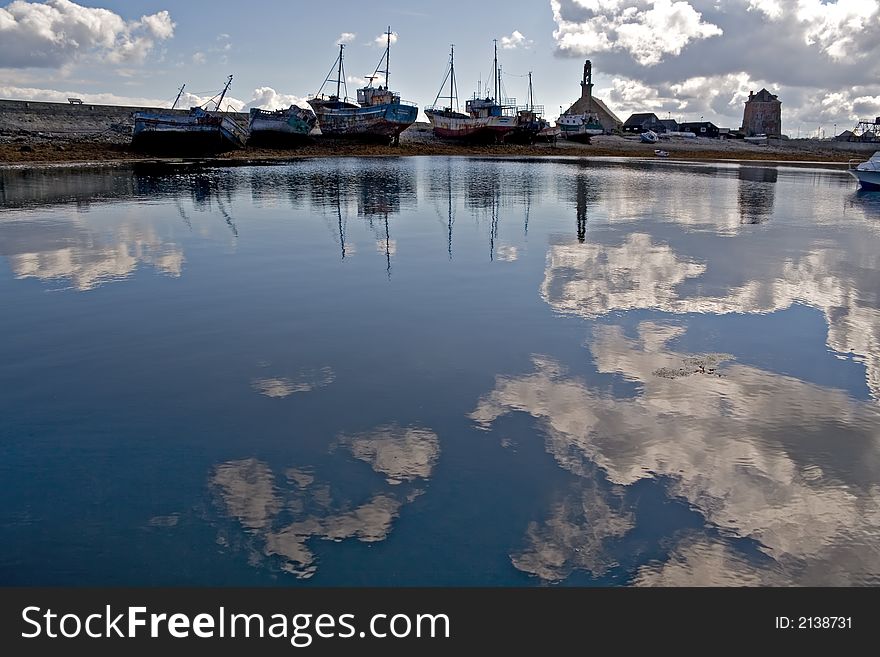 Blue water reflecting the clouds, with old harbor and boat silhouettes. Blue water reflecting the clouds, with old harbor and boat silhouettes