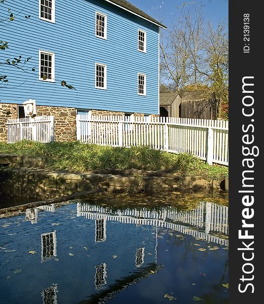 A historic blue mill reflects off the water. A historic blue mill reflects off the water.