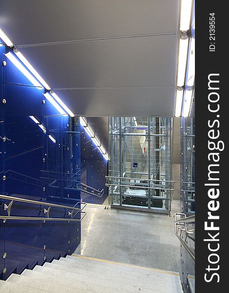 Stairway with walls of blue glass banisters and fastening units of polished steel. In the background the elevator-housing. Stairway with walls of blue glass banisters and fastening units of polished steel. In the background the elevator-housing