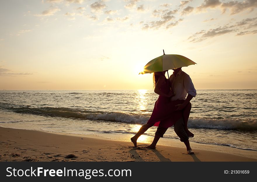 Couple kissing under umbrella at the beach in sunset. Couple kissing under umbrella at the beach in sunset.