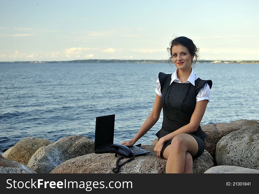 Office by the sea: the girl on the rocks with a laptop and a desktop phone. space for text