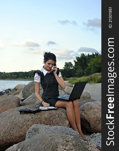 Office by the sea: the girl on the rocks with a laptop and a desktop phone signing papers