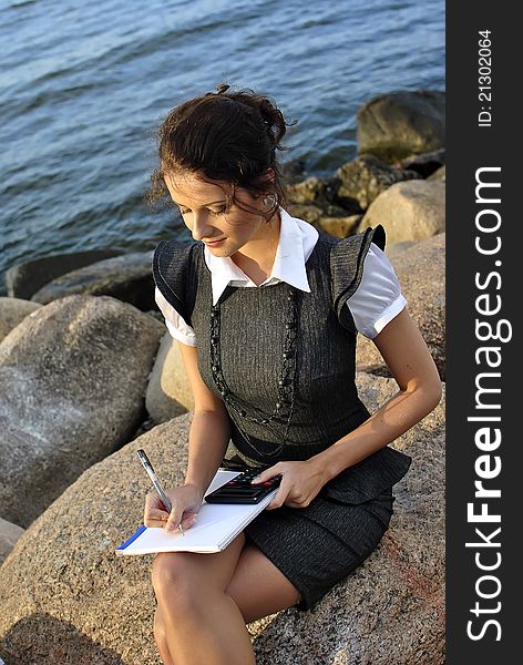 Beautiful girl with a notebook and a calculator sitting on the rocks