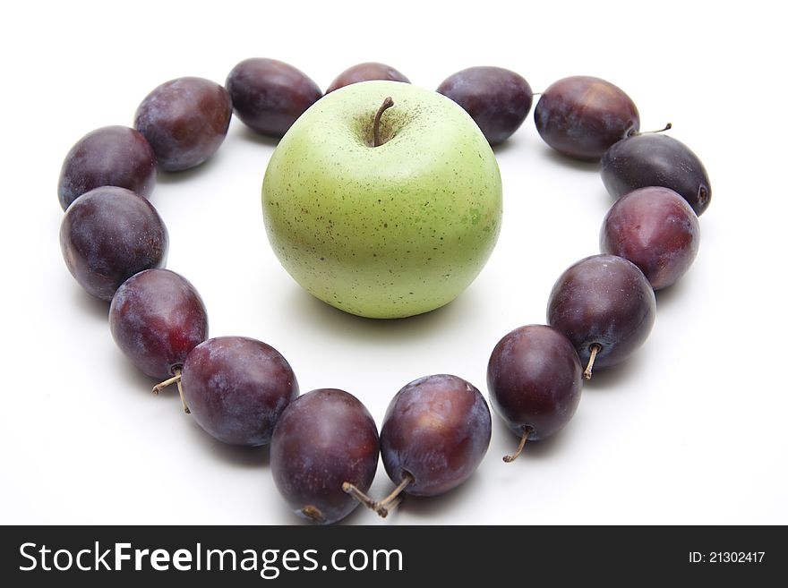 Plums with apple in heart form on white background