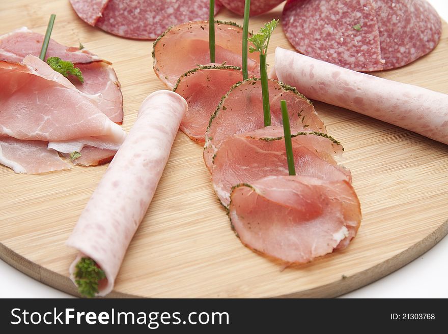 Ham with salami and herbs on wooden plate