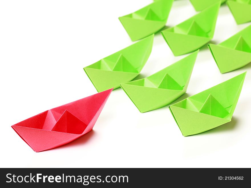 One red and several green paper boats on white background. One red and several green paper boats on white background