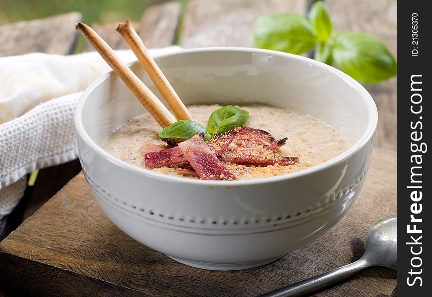 A bowl of mushroom soup with bacon and basil. Selective focus