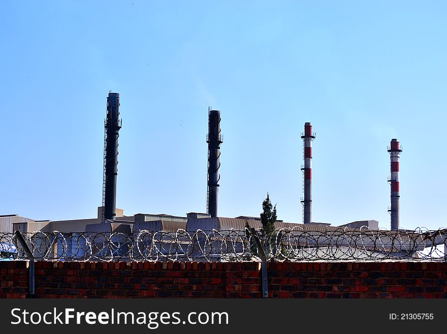A factory with chimneys behind a wall with barbed wire on it. A factory with chimneys behind a wall with barbed wire on it.