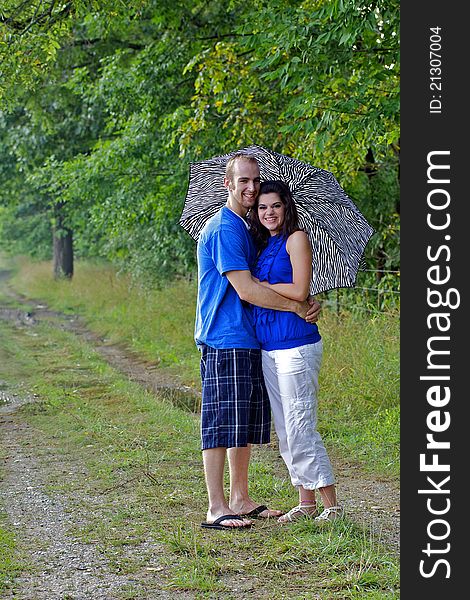 Couple in farm field with arms around each other holding an umbrella. Couple in farm field with arms around each other holding an umbrella