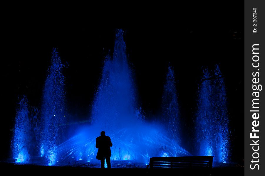 Male standing in front of a beautiful water feature fountain at night. Male standing in front of a beautiful water feature fountain at night